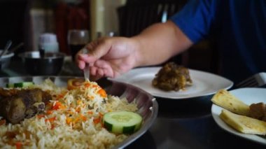 Nasi Mandhi 'yi yemek için seçen yakın çekim elleri bu lezzetli yemeği seçip beğenmenin mahrem eylemini sergiliyor. Nasi mandhi, mis kokulu ve zengin lezzetleriyle bilinen geleneksel bir Orta Doğu pirinç yemeğidir..