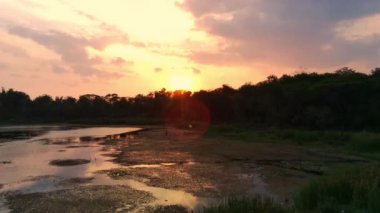 Surabaya, Endonezya 'da günbatımı sırasında tepelerde ağaçlarla çevrili küçük gölet manzarası. Drone Görüntüsü