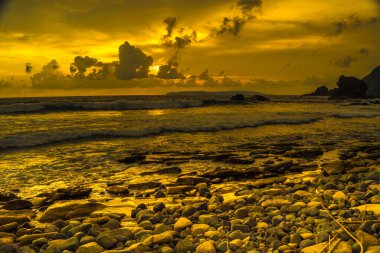 Papuma, Jember, Doğu Java, Endonezya 'daki kayalık sahilde gün batımı. Okyanus dalgalarıyla dolu bulutlu bir öğleden sonra kumları aşındırıyor. Doğa ve Manzara Fotoğrafçılığı.