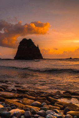 Papuma, Jember, Doğu Java, Endonezya 'daki kayalık sahilde gün batımı. Okyanus dalgalarıyla dolu bulutlu bir öğleden sonra kumları aşındırıyor. Doğa ve Manzara Fotoğrafçılığı.