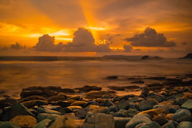 Papuma, Jember, Doğu Java, Endonezya 'daki kayalık sahilde gün batımı. Okyanus dalgalarıyla dolu bulutlu bir öğleden sonra kumları aşındırıyor. Doğa ve Manzara Fotoğrafçılığı.