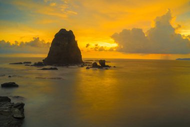 Papuma, Jember, Doğu Java, Endonezya 'daki kayalık sahilde gün batımı. Okyanus dalgalarıyla dolu bulutlu bir öğleden sonra kumları aşındırıyor. Doğa ve Manzara Fotoğrafçılığı.