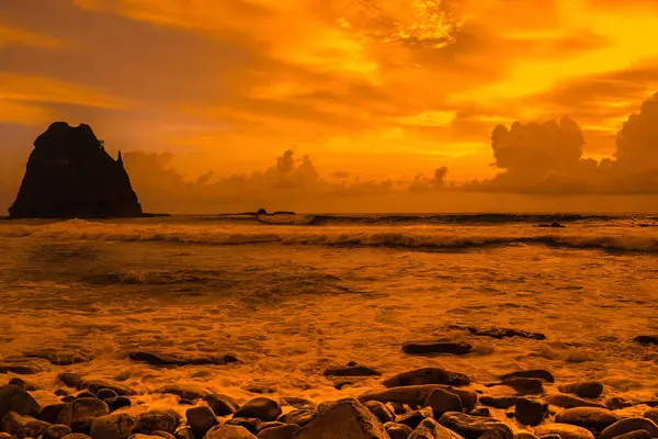 Papuma, Jember, Doğu Java, Endonezya 'daki kayalık sahilde gün batımı. Okyanus dalgalarıyla dolu bulutlu bir öğleden sonra kumları aşındırıyor. Doğa ve Manzara Fotoğrafçılığı.