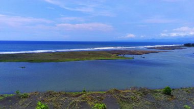 Endonezya 'nın doğusunda, Jember, Doğu Java' da, berrak bir mavi gökyüzü altında yumuşak dalgalar altında dalgalanan, yemyeşil bir adaya sahip sakin bir deniz manzarası..