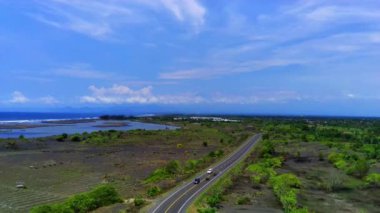 JLS 'de ya da Endonezya' nın Jember kentindeki güney kıyı şeridinde uzun bir kıyı yolu. Gök mavisi okyanusun uçsuz bucaksızlığıyla gölgelenmiş.