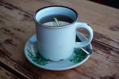 Limon çimi dilimli dumanı tüten bir çay teneke bir fincanın üzerinde, gümüş bir kaşık eşliğinde kırsal ahşap bir masada duruyor..