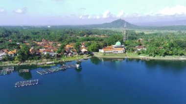 Arka planda kubbe ve uzun minareli beyaz camili sakin bir göl manzarası. Bereketli yeşillik gölü çevrelemektedir. Ranu Pakis yakınlarında, Lumajang, Doğu Java, Endonezya.