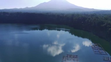 Kristal berrak bir göl dramatik bir dağ sırasını yansıtır. Ranu Pakis, Lumajang, Doğu Java, Endonezya yakınlarındaki yemyeşil orman etrafını sarar.
