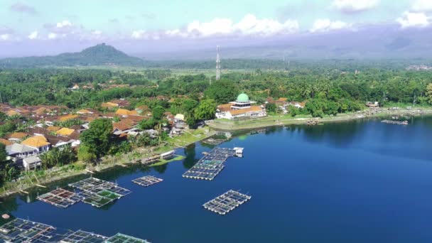 无人机视频拍摄了位于印度尼西亚东爪哇鲁马扬Ranu Pakis湖畔的一个风景秀丽的村庄 茂密的绿叶环绕着五颜六色的古屋 烟囱里冒出的浓烟卷曲 预示着一种宁静的生活 — 图库视频影像