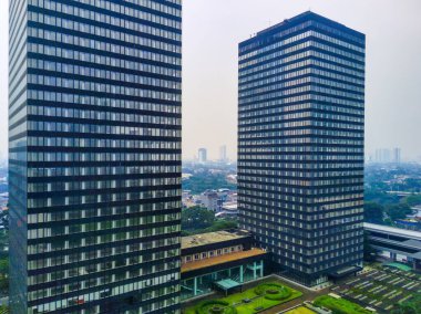Sudirman Caddesi, Jakarta 'da iki gökdelenin manzarası. Gökdelenlerin birçok penceresi vardır ve ağaçlar ve diğer binalarla çevrilidir. Hava Fotoğrafçılığı.