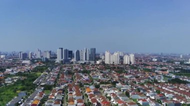 İnsansız hava aracı Surabaya şehri ve yerleşim alanının görüntülerini alıyor. İnsansız hava aracı, yüksek binalar ve ağaçlarla çevrili evleri olan bir mahallede uçuyor..