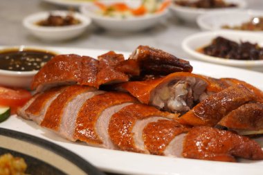 Kızarmış ördeğin beyaz bir tabakta çıtır çıtır derisi olan yakın plan fotoğrafı. Koyu bir sos ve dilimlenmiş soğanla servis edilir..