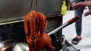Bir insan büyük, yuvarlak bir tavada bütün bir ördeğin üzerine sıcak yağ döküyor, derisi çıtır çıtır ve altın kahverengiye dönüyor..