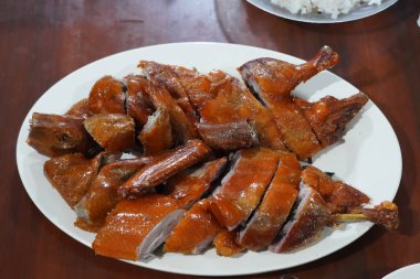 Kızarmış ördek göğsü, beyaz bir tabakta. Ördek derisi kahverengi ve çıtır çıtır. Susam tohumları ve doğranmış yeşil soğan serpiştirilmiş..