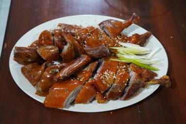 a roasted duck breast on a white plate. The duck skin is brown and crispy, and it is sprinkled with sesame seeds and chopped green onions. clipart