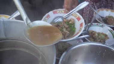 Soto Iga 'nın bir kepçesini çömlekten bir kaseye döken bir adam. Soto Iga, Endonezya 'nın Surabaya kentinde popüler bir et çorbası türüdür. Biftek ve et suyundan yapılır.