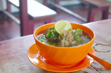 Hafif ahşap bir masada pirzola çorbasıyla dolu bir kase. Bir kireç parçası kasenin kenarında duruyor..