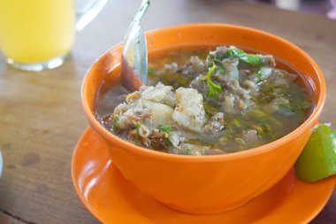 Hafif ahşap bir masada pirzola çorbasıyla dolu bir kase. Bir kireç parçası kasenin kenarında duruyor..