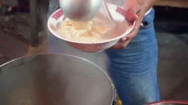 Bir insan, Endonezya kuzu çorbası ya da Sop Kambing Betawi restoranında kepçe kepçesiyle yemek yer..