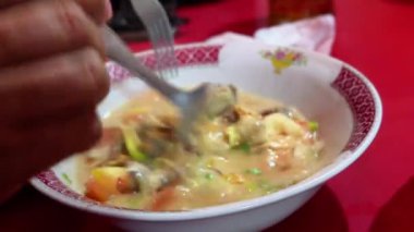 Bir insan, Endonezya kuzu çorbası ya da Sop Kambing Betawi restoranında kepçe kepçesiyle yemek yer..