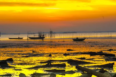 Gün batımında Endonezya, Madura, Bangkalan 'da sakin bir sahilde küçük bir ahşap tekne dinlenir. Ateşli gökyüzü kıyıda huzur içinde otururken suya yansıyor..
