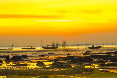 Bangkalan, Madura, Doğu Java 'da güzel bir gün batımı. Canlı turuncu gökyüzüne karşı siluetlenmiş iki tekne suyun üzerinde hafifçe sallanıyordu. Kumsal boş ve huzurlu..