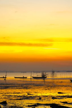 Bangkalan, Madura, Doğu Java 'da güzel bir gün batımı. Canlı turuncu gökyüzüne karşı siluetlenmiş iki tekne suyun üzerinde hafifçe sallanıyordu. Kumsal boş ve huzurlu..