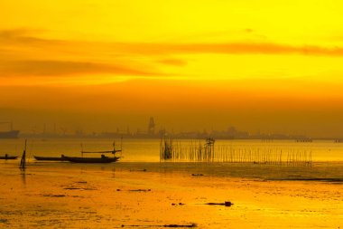 A beautiful sunset over a beach in Bangkalan, Madura, East Java. Silhouetted against the vibrant orange sky are two boats bobbing gently on the water. The sandy beach is empty and peaceful. clipart