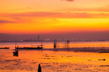 Bangkalan, Madura, Doğu Java 'da güzel bir gün batımı. Canlı turuncu gökyüzüne karşı siluetlenmiş iki tekne suyun üzerinde hafifçe sallanıyordu. Kumsal boş ve huzurlu..
