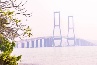 The Suramadu Bridge, the longest bridge in Indonesia, stretches across the Madura Strait during a foggy day clipart