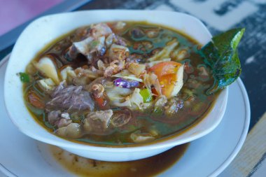 A bowl of Tongseng, Indonesian traditional food with chunks of meat, vegetables, and spices in a rich broth, topped with fried shallots and chili peppers. clipart