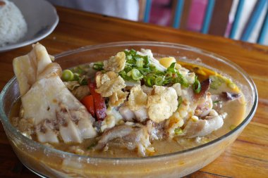 A bowl of collagen savory cow feet Indonesian soup with meat, vegetables, and crispy crackers. clipart