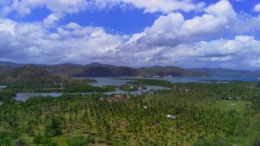 Lombok, Endonezya 'daki Cemare Sahili' nin nefes kesici hava manzarası, bereketli bir hindistan cevizi plantasyonu, sakin bir koy ve dramatik bir gökyüzü altında görkemli dağlar..