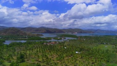 Lombok, Endonezya 'daki Cemare Sahili' nin nefes kesici hava manzarası, bereketli bir hindistan cevizi plantasyonu, sakin bir koy ve dramatik bir gökyüzü altında görkemli dağlar..