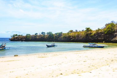 Lombok, Endonezya 'da Pink Beach yakınlarında el değmemiş bir sahil manzarası. Turkuaz berrak sular beyaz kumlu kıyıya doğru yol alırken renkli balıkçı tekneleri körfezde hafifçe sallanıyor.