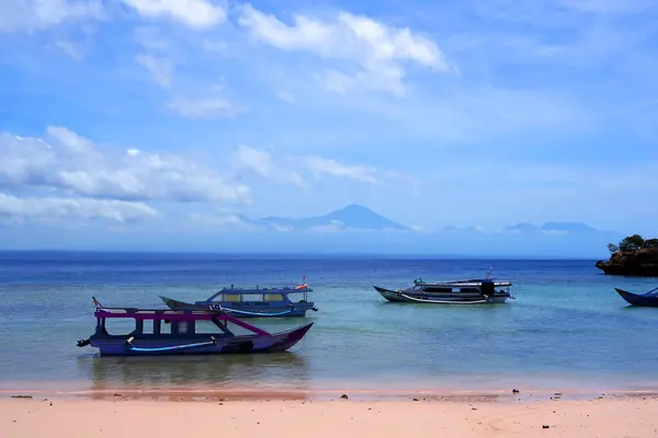 Lombok, Endonezya 'da Pink Beach yakınlarında el değmemiş bir sahil manzarası. Turkuaz berrak sular beyaz kumlu kıyıya doğru yol alırken renkli balıkçı tekneleri körfezde hafifçe sallanıyor.