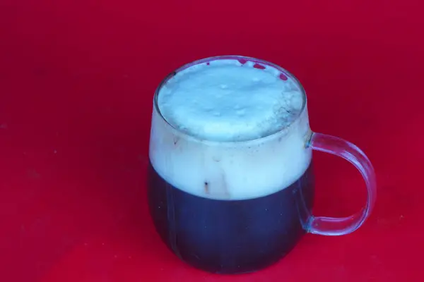 stock image A glass of chocolate milk with a sheen sits on a red background. in studio.