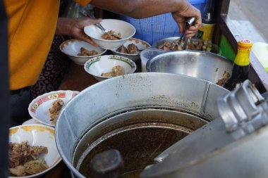 Surabaya, Endonezya 'daki bir sokak yemeği satıcısı çorba kaselerine pişmiş sığır pirzolası ekliyor. Satıcı, renkli desenlerle süslenmiş kaburgaları dikkatlice kaselere yerleştirmek için maşa kullanıyor..
