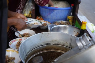 Surabaya, Endonezya 'daki bir sokak yemeği satıcısı çorba kaselerine pişmiş sığır pirzolası ekliyor. Satıcı, renkli desenlerle süslenmiş kaburgaları dikkatlice kaselere yerleştirmek için maşa kullanıyor..