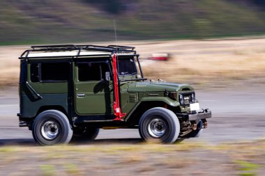 3 Kasım 2024. Bromo, Doğu Java, Endonezya. Klasik bir Toyota Land kruvazörü FJ40 yuvarlanan tepeler ve çayırlarla manzaralı bir arazide ilerliyor..