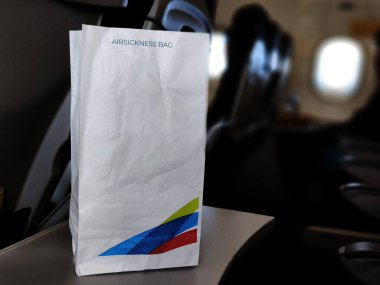 An airsickness bag with a colorful airline logo rests on an airplane seatback tray. clipart