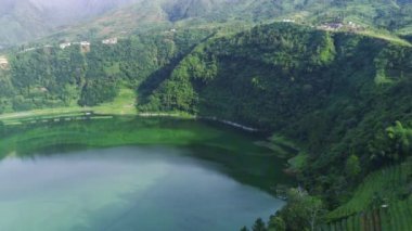 Telaga Menjer, Wonosobo 'nun nefes kesici hava manzarası. Etrafı yemyeşil ormanlarla, çay tarlalarıyla çevrili sakin bir göl ve yuvarlanan tepelerin arasına yerleşmiş dağınık konaklama yerleri sergiliyor..