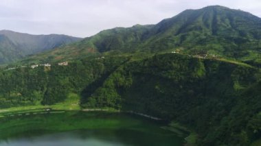 Telaga Menjer, Wonosobo 'nun nefes kesici hava manzarası. Etrafı yemyeşil ormanlarla, çay tarlalarıyla çevrili sakin bir göl ve yuvarlanan tepelerin arasına yerleşmiş dağınık konaklama yerleri sergiliyor..