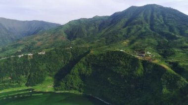 Telaga Menjer, Wonosobo 'nun nefes kesici hava manzarası. Etrafı yemyeşil ormanlarla, çay tarlalarıyla çevrili sakin bir göl ve yuvarlanan tepelerin arasına yerleşmiş dağınık konaklama yerleri sergiliyor..