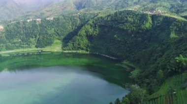 Telaga Menjer, Wonosobo 'nun nefes kesici hava manzarası. Etrafı yemyeşil ormanlarla, çay tarlalarıyla çevrili sakin bir göl ve yuvarlanan tepelerin arasına yerleşmiş dağınık konaklama yerleri sergiliyor..