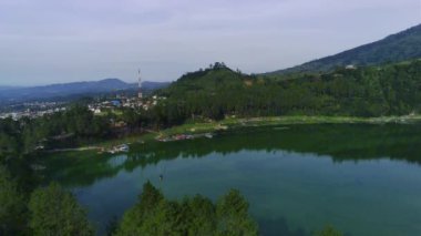 Telaga Menjer, Wonosobo 'nun nefes kesici hava manzarası. Etrafı yemyeşil ormanlarla, çay tarlalarıyla çevrili sakin bir göl ve yuvarlanan tepelerin arasına yerleşmiş dağınık konaklama yerleri sergiliyor..