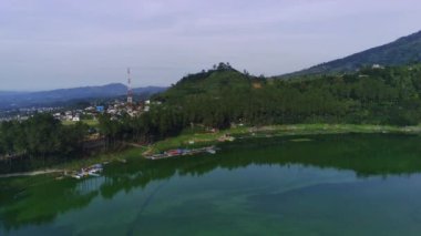 Telaga Menjer, Wonosobo 'nun nefes kesici hava manzarası. Etrafı yemyeşil ormanlarla, çay tarlalarıyla çevrili sakin bir göl ve yuvarlanan tepelerin arasına yerleşmiş dağınık konaklama yerleri sergiliyor..
