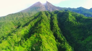 Endonezya 'nın en aktif volkanı Merapi Dağı' nın havadan görünüşü. Simetrik konisi, yemyeşil yamaçlar ve açık mavi gökyüzü ile çelişen bir duman bulutu ile kaplıdır..