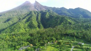 Merapi Dağı 'nın görkemli manzarası, Endonezya' nın merkezindeki aktif bir volkan. Zirvesinden yükselen duman gücünü ve güzelliğini gözler önüne seriyor. Yemyeşil bitki örtüsü yamaçları kaplıyor.