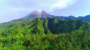 Merapi Dağı 'nın görkemli manzarası, Endonezya' nın merkezindeki aktif bir volkan. Zirvesinden yükselen duman gücünü ve güzelliğini gözler önüne seriyor. Yemyeşil bitki örtüsü yamaçları kaplıyor.